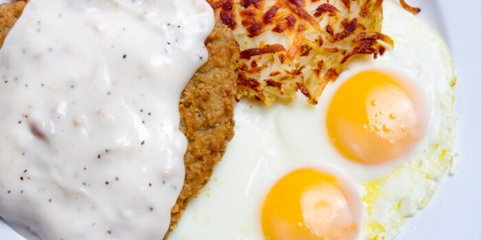 Two sunny-side-up eggs, hash browns, and breaded steak at New Brighton Bar on a plate.