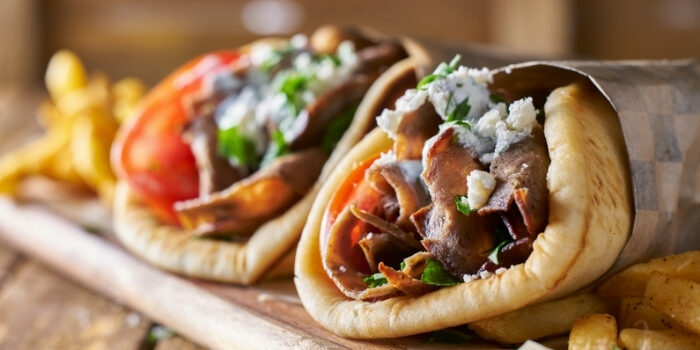Two gyros in pita with veggies, meat, and cheese, served with fries at New Brighton Restaurant.