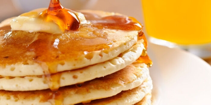 Stack of pancakes with butter and syrup at Fifth Avenue Taphouse New Brighton, OJ in back.