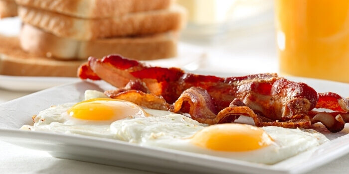 Two sunny-side-up eggs and crispy bacon at Fifth Avenue Taphouse New Brighton with toast and juice.